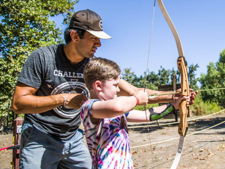 A camper learning how to shoot a bow and arrow.